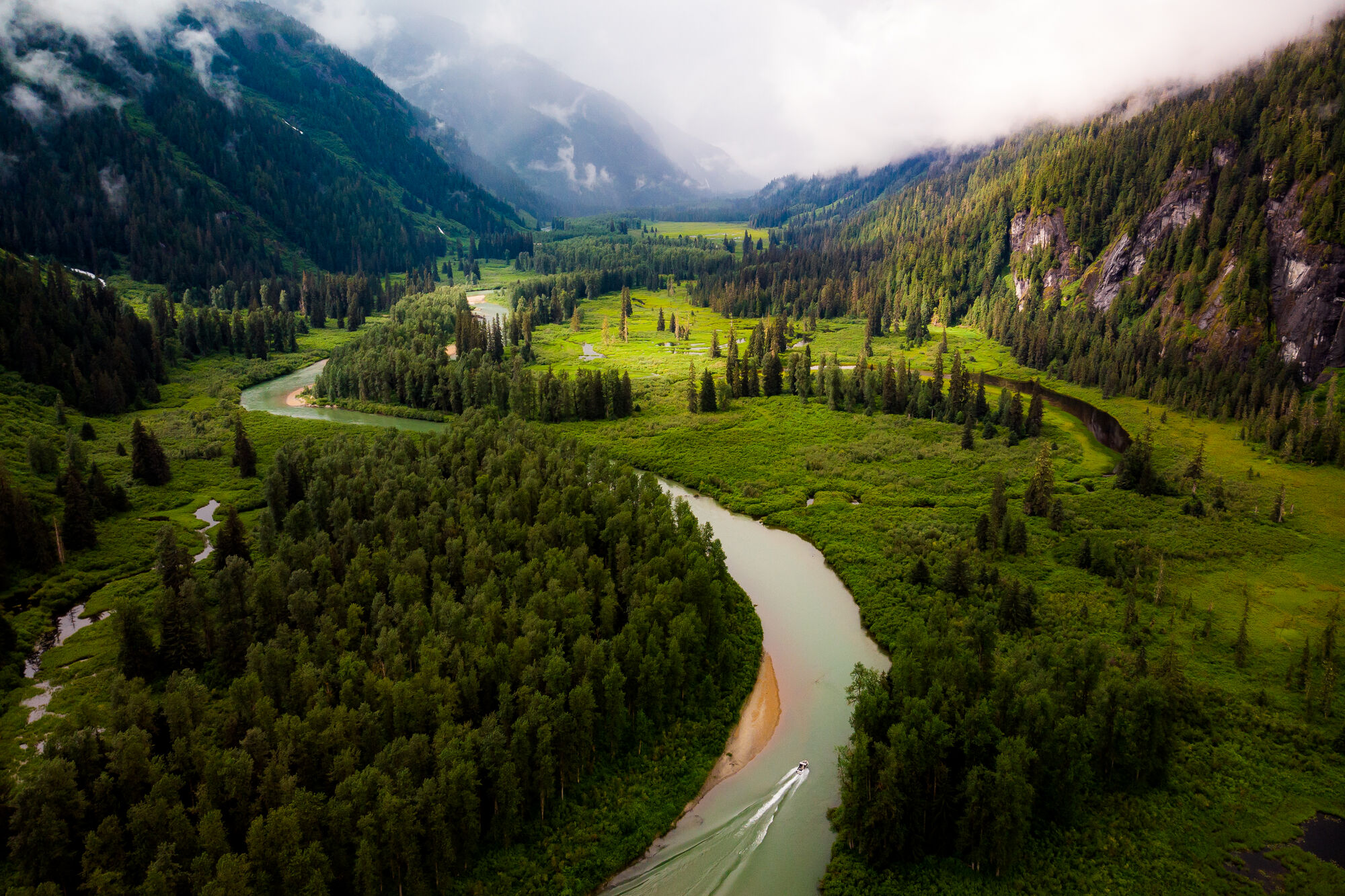 A river runs through a verdant green valley with misty mountains in the distance